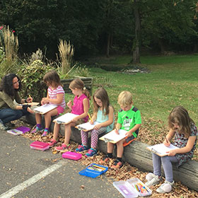 Group of children drawing with a teacher outside.